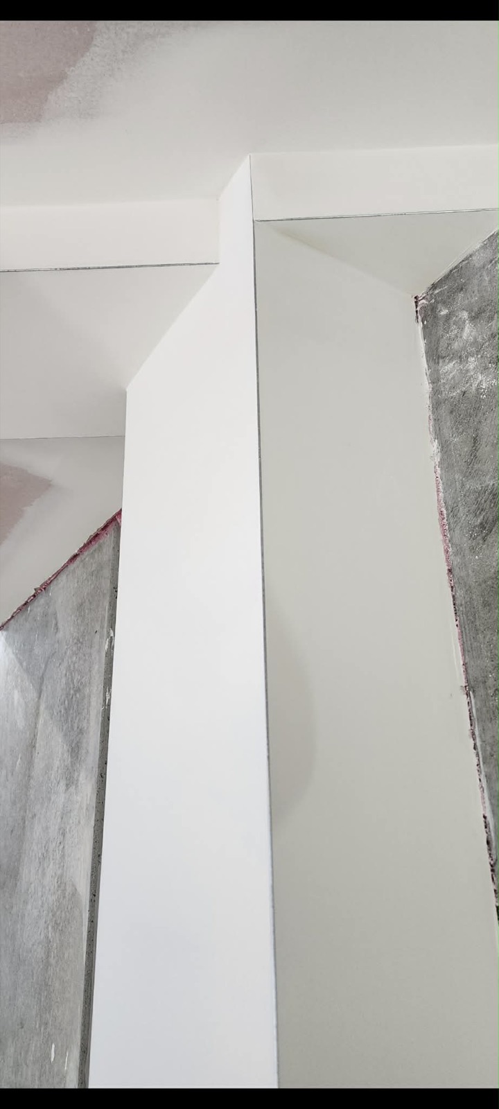 Sharp plastered column return beside exposed concrete walls.